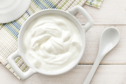 plain yogurt, in a porcelain bowl, with a porcelain spoon next to it, on a wooden table