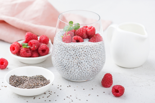 chia  pudding with raspberries on top, the ingredients milk and chia seeds and raspberries aside, on a kitchen table