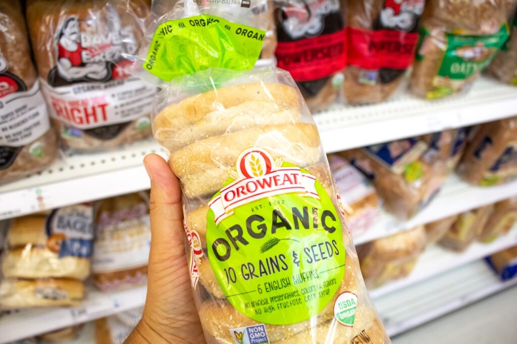 a customer holds a bag of oroweat english muffins at the grocery store, in front of oroweat store front