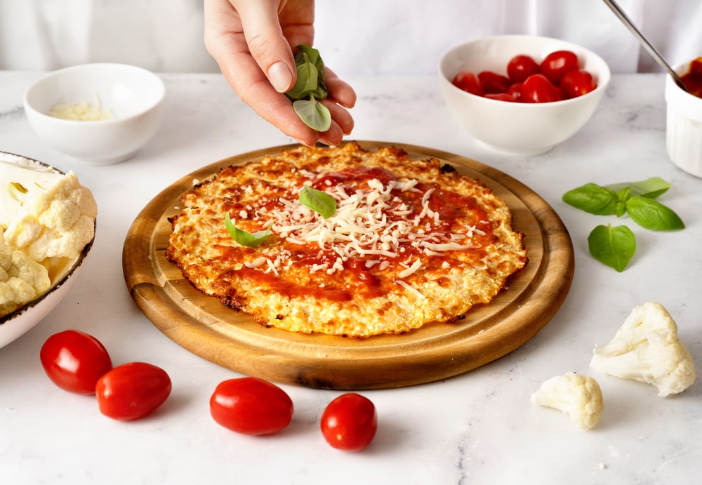 freshly-baked keto pizza, with a cheese crust, topped with cherry tomatoes and mozzarella cheese, evenly distributed toppings on a golden brown crust, served on a wooden plate, hot and ready to be enjoyed