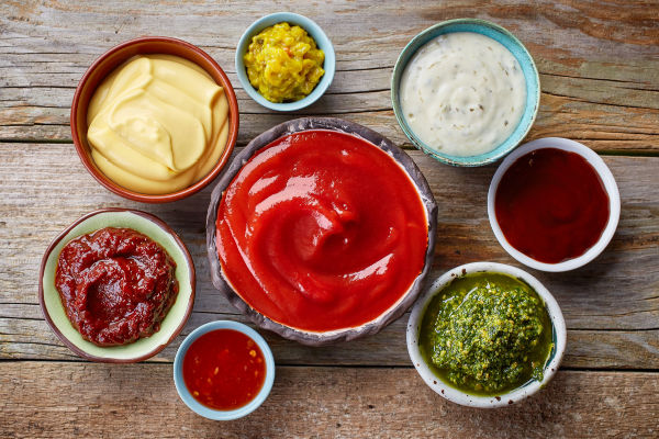 A selection of condiments arranged in small bowls on a wooden table.