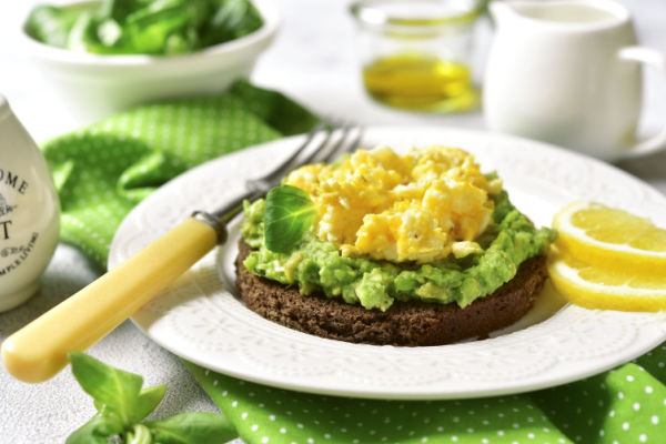 A plate with a cake topped with smashed avocado and scrambled egg.