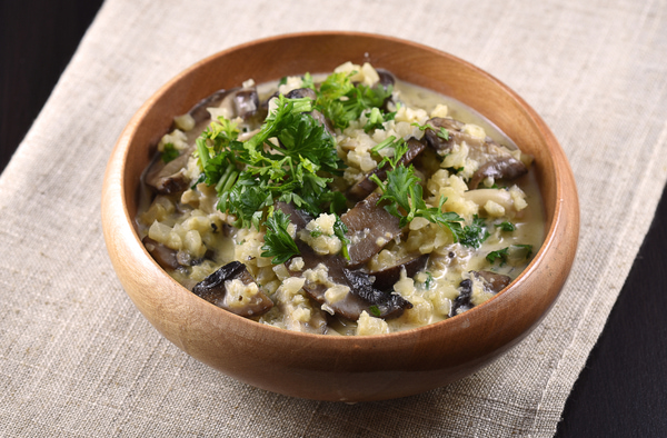 Cauliflower risotto with mushroom topped with parsley in a wooden bowl
