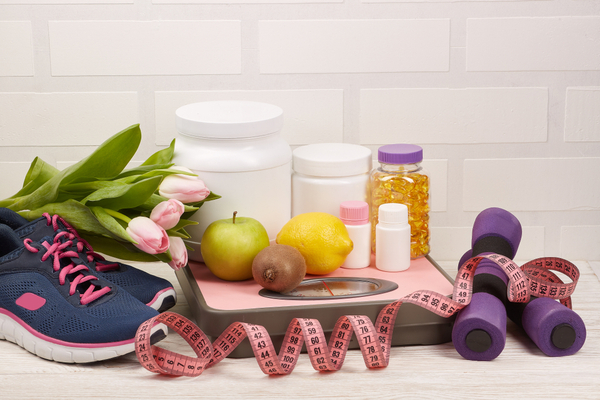 Keto OS NAT Before and After: The Best Fat-Burning Boost? 2 Sports nutrition supplements and various fruits on a weighing scale with fitness and health accessories