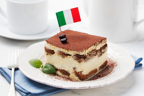 Slice of tiramisu cake on a plate with Italian flag on top