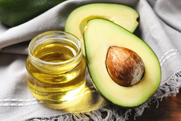 A photo of an avocado and a jar of avocado oil, arranged side by side.