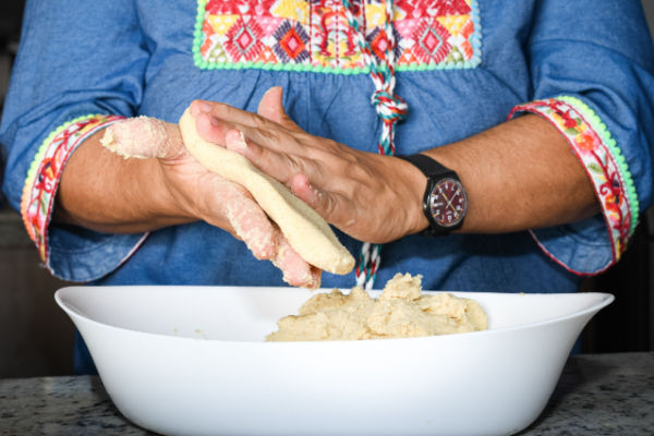 A woman's hands holding a small ball of cauliflower tortilla mixture and flattening it into a thin round shape.