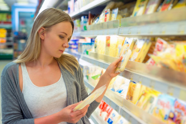 A photo of a woman standing in front of a display of cheeses at Costco, carefully examining the different types of cheese.