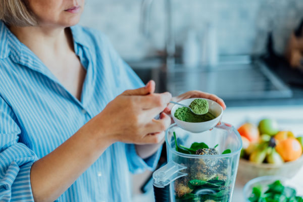 Keto Smoothie King Hacks: How to Customize Low-Carb Drink 5 A woman skillfully creating a homemade green smoothie, with a colorful assortment of green ingredients, including spinach, kale, avocado, cucumber, and fresh herbs.