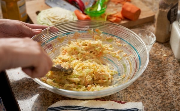 Keto Coleslaw Done Right: Crunchy, Creamy, and Low-Carb! 5 A person mixing a coleslaw in a glass bowl