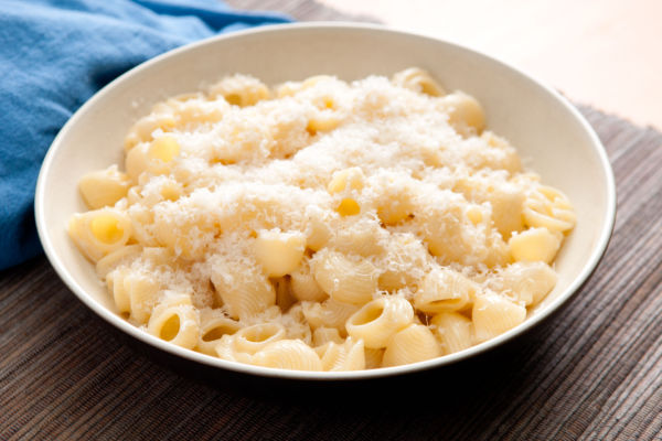 A plate of pipe or shell pasta covered in a creamy Alfredo sauce, garnished with grated Parmesan cheese.