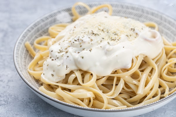 A plate of noodles generously coated in creamy Alfredo sauce.
