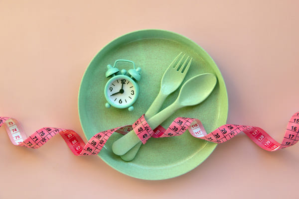 Concept for fasting with an empty plate, spoon & fork, alarm clock, and measuring tape