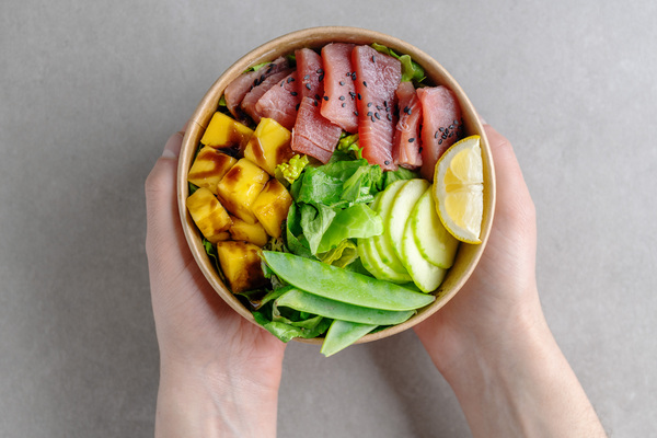 Perfect Subway Protein Bowl: The Ultimate Guide 10 A young man holding a healthy raw tuna bowl with a variety of vegetables. The bowl contains fresh raw tuna, vegetables, and a bed of greens, creating a nutritious meal.