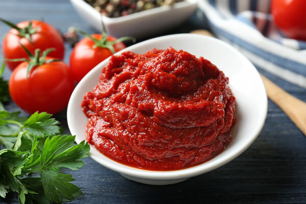 Tomato paste in a bowl with tomatoes and herbs