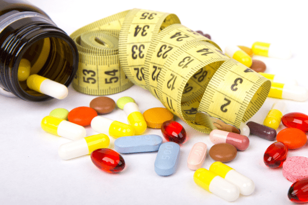 Is the One Shot Keto Diet Safe and Effective? Unraveling the Facts 2 Pills arranged next to a tape measure, illustrating the concept of medication management and health measurement.