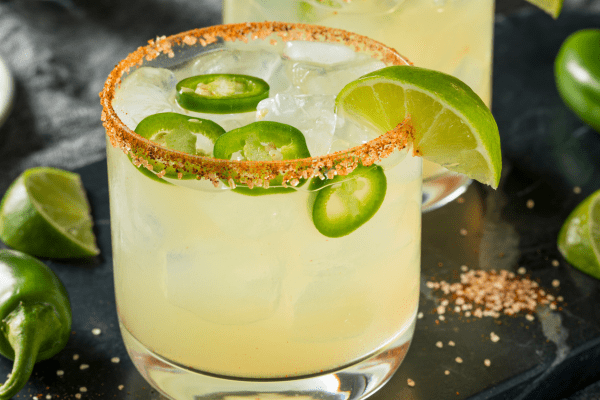 Margarita cocktail in a glass featuring a prominent spicy salt rim, a slice of jalapeno, and a lime wedge garnish, offering a spicy twist on the classic drink.