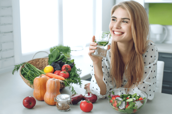A scene depicting a woman drinking water while eating salads and vegetables, deep in thoughts on how long does it take to go into ketosis.