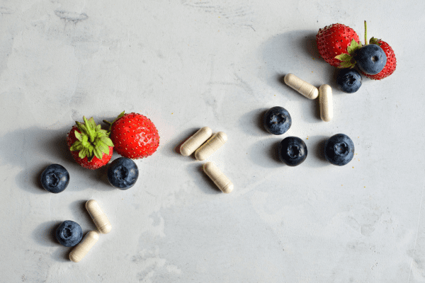 Is the One Shot Keto Diet Safe and Effective? Unraveling the Facts 8 Pills scattered alongside strawberries and berries, illustrating a blend of medication and nutritious fruits.