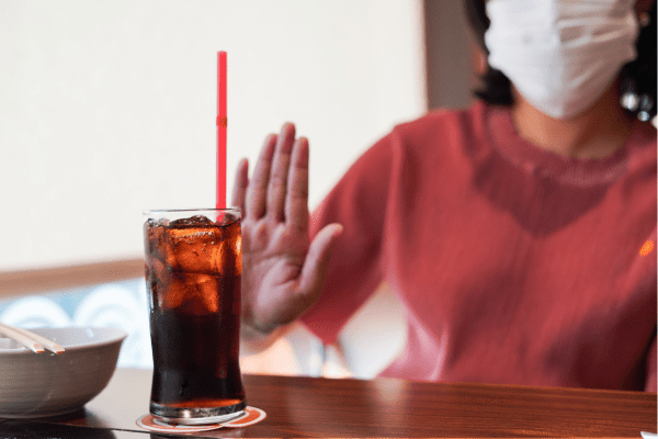 A photo of a woman gesturing a refusal towards a soft drink, indicating her preference not to consume sugary beverages.