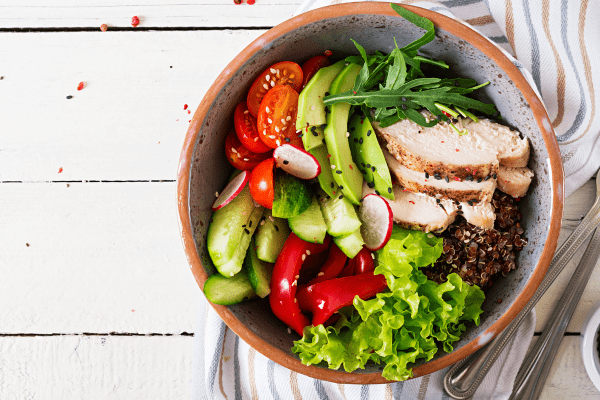 A bowl filled with a delicious combination of ingredients, including avocado, lettuce, fresh tomatoes, chicken, and various other toppings.