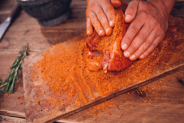 A piece of meat being generously seasoned with a flavorful mix of herbs and spices.