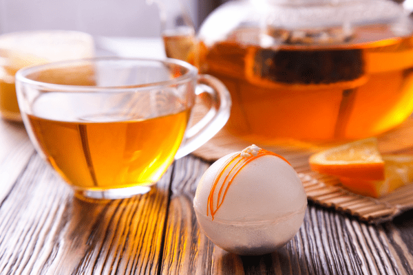 A cup of tea with a tea bomb placed next to it.