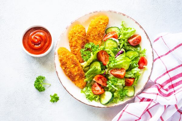 A plate of salad with chicken nuggets and sauce