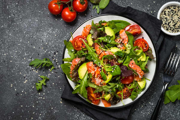 Greek salmon salad with avocado, tomato, green leaves, and sesame seeds