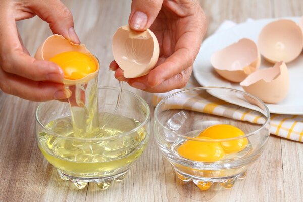 Hands separating egg whites and yolks into two bowls