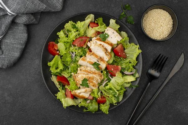 Sliced chicken breast with tomatoes served on a bed of fresh lettuce and placed on a black plate