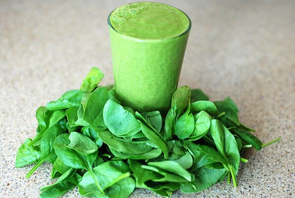 A glass of green smoothie with fresh spinach