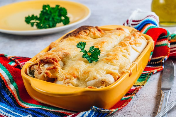A cheesy enchilada with herb on top and served in a yellow tray