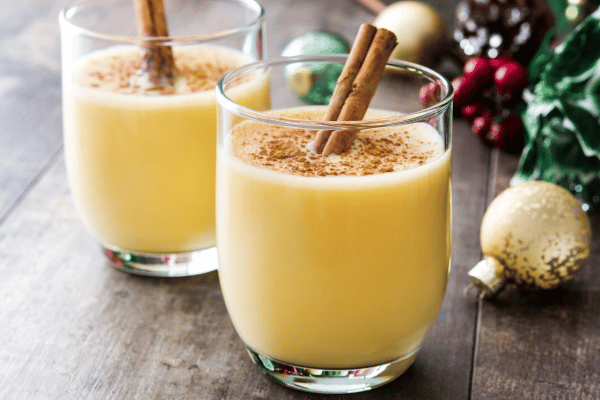 Keto Eggnog 101: A Complete Recipe Guide for the Holidays 9 Eggnog served in two clear glasses, garnished with cinnamon sticks, presenting a festive and inviting holiday beverage arrangement.
