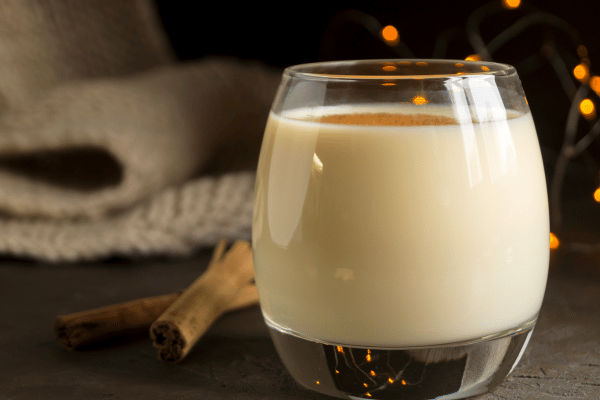 Keto Eggnog 101: A Complete Recipe Guide for the Holidays 7 A delicious glass of eggnog with a touch of festivity, adorned with cinnamon sticks on the side, promising a delightful and flavorful holiday treat.