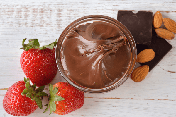 Sugar Free Nutella: Satisfy Your Sweet Tooth Guilt Free 5 A tempting bowl of chocolate hazelnut spread with fresh strawberries, chocolate, and nuts, presenting a delightful combination of flavors and textures.