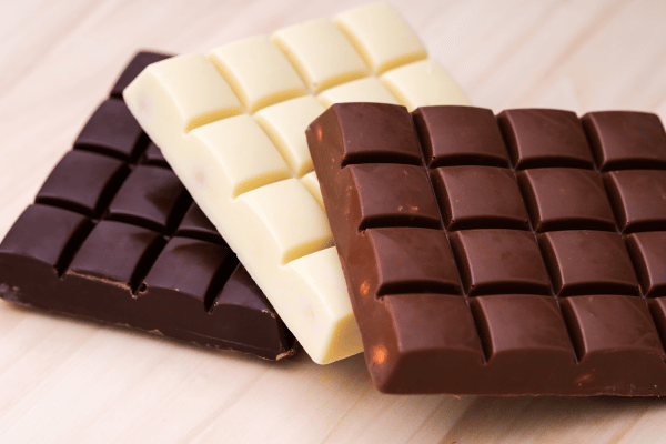 An assortment of chocolate bars, including milk chocolate, dark chocolate, and white chocolate, are elegantly displayed on a wooden background, offering a delectable variety for every chocolate lover.