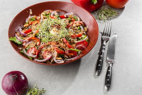 Bowl of fresh Italian salad with onion, red pepper, and utensils on the side