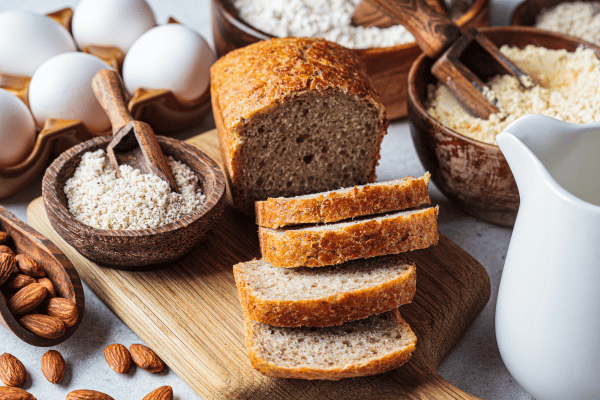 Is L Oven Fresh Keto Bread Worth the Hype? 3 Keto Bread on a wooden board with different types of low-carb flour surrounding it.