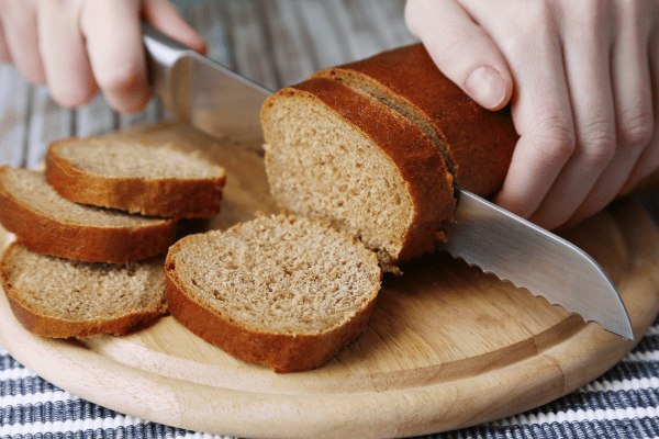 Is L Oven Fresh Keto Bread Worth the Hype? 4 A Close Up Image of Female Hands Cutting Bread on Wooden Board.