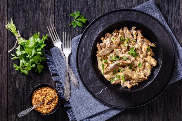 Keto Beef Stroganoff: Taste the Victory in Every Dish! 9 A bowl of beef stroganoff with utensils and herbs on the side