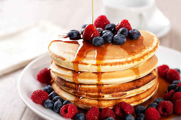 A stack of pancakes with maple syrup and fresh berries