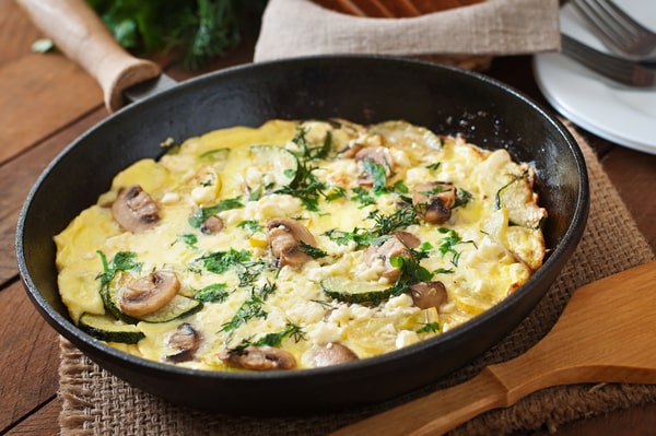 Mushroom Frittata Recipe: Quick and Easy Meal You’ll Love 3 A mushroom frittata and cheese, garnished with fresh herbs, served in a skillet with a wooden spatula nearby on a rustic table