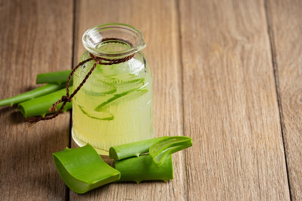 19 Homemade Drinks That Burn Fat While Sleeping: Find Out! 4 A glass bottle filled with aloe vera juice, accompanied by fresh aloe vera leaves, placed on a wooden surface