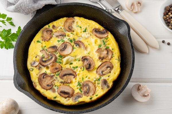 Mushroom Frittata Recipe: Quick and Easy Meal You’ll Love 4 A savory frittata with mushrooms and herbs, served in a cast iron skillet, surrounded by fresh ingredients and utensils on a white wooden background