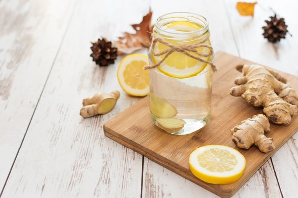 19 Homemade Drinks That Burn Fat While Sleeping: Find Out! 7 A jar of detox water infused with slices of lemon and ginger, placed on a wooden cutting board, surrounded by fresh ginger roots and lemon slices on a rustic wooden background