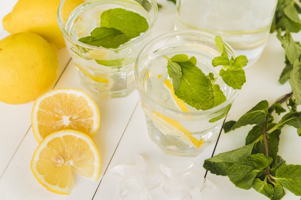 19 Homemade Drinks That Burn Fat While Sleeping: Find Out! 9 Two glasses of refreshing lemon water with mint leaves, surrounded by fresh lemons and mint sprigs