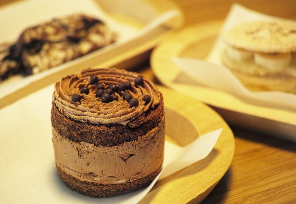 A close-up of a beautifully decorated chocolate mousse cake topped with chocolate chips, placed on a wooden plate