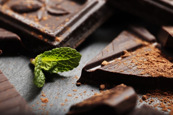 Quest Bars Keto: Your Go-to Snack for Weight Loss 10 Close-up of broken dark chocolate pieces dusted with cocoa powder, accompanied by a fresh mint leaf