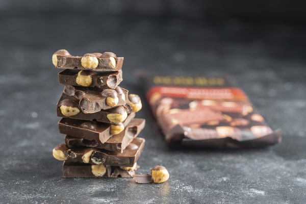 Quest Bars Keto: Your Go-to Snack for Weight Loss 11 A stack of chocolate pieces with whole hazelnuts, placed on a gray surface with a blurred chocolate packaging in the background